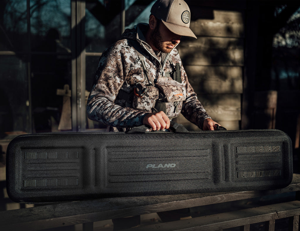 Person in camouflage gear opening a black PLAND case outdoors.