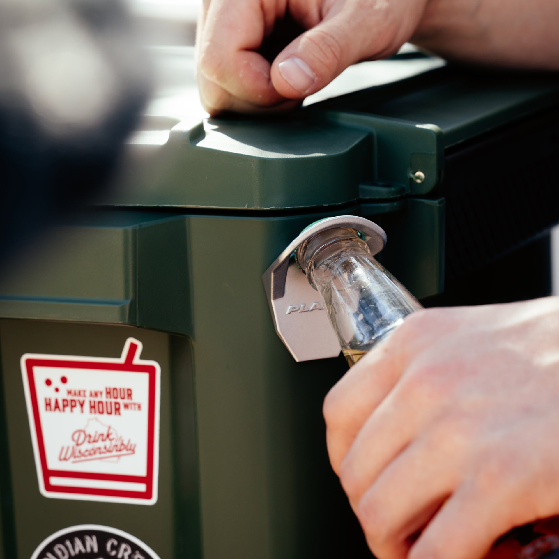 Person opening a bottle using a green outdoor kitchen appliance with a 'Happy Hour' sticker.