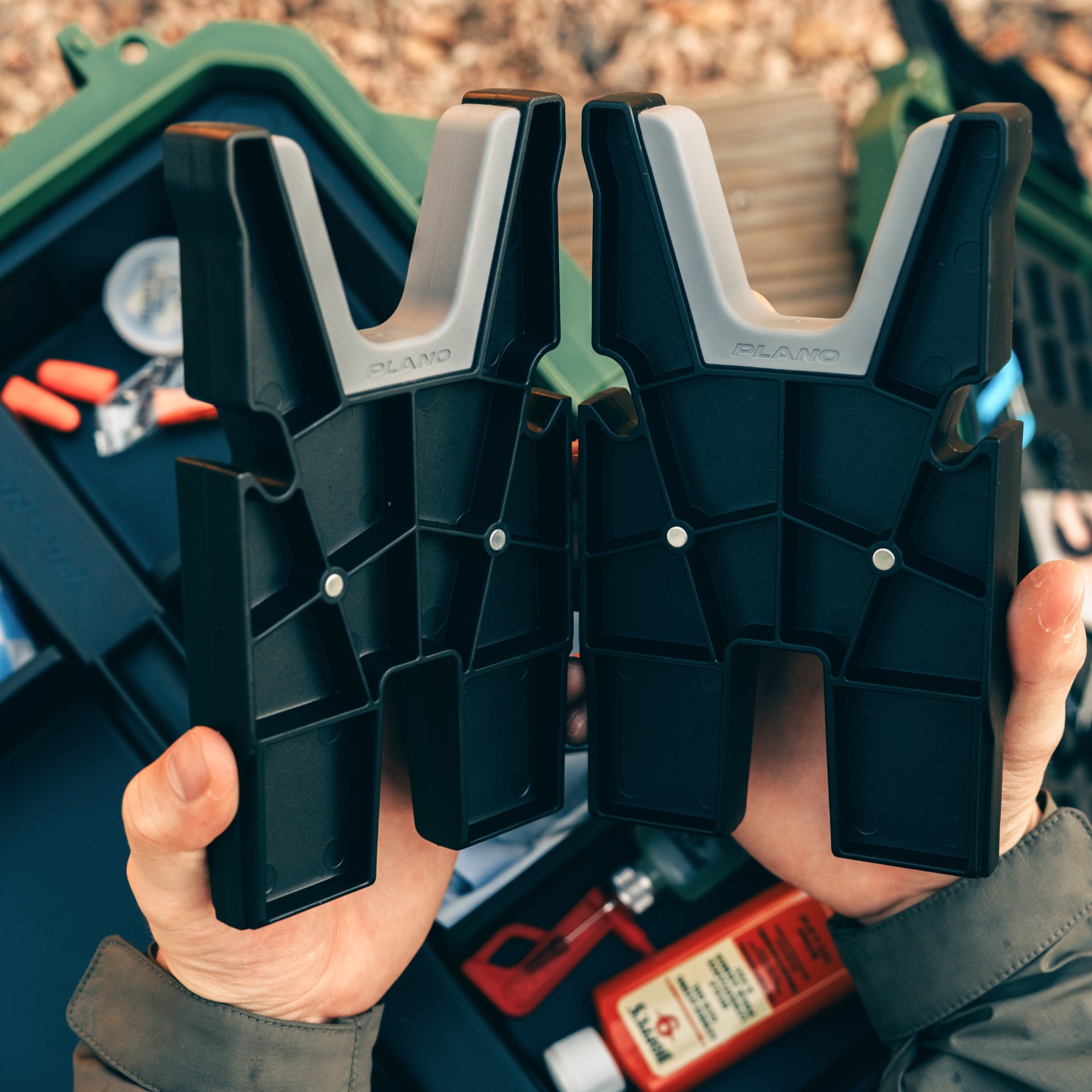 Two black and gray clamps held by a person with a toolbox in the background
