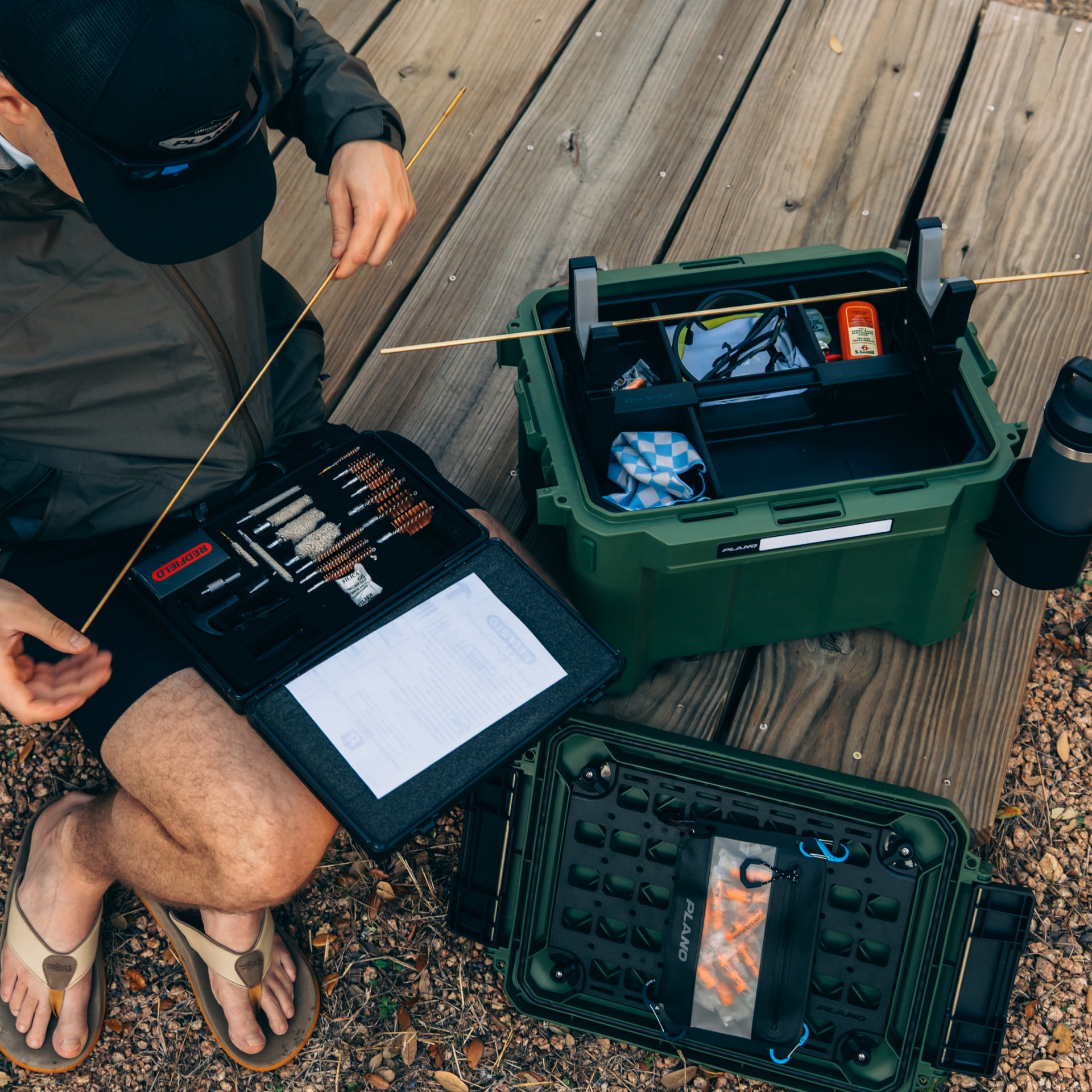 Person sitting on a wooden deck with fishing gear and tackle boxes.
