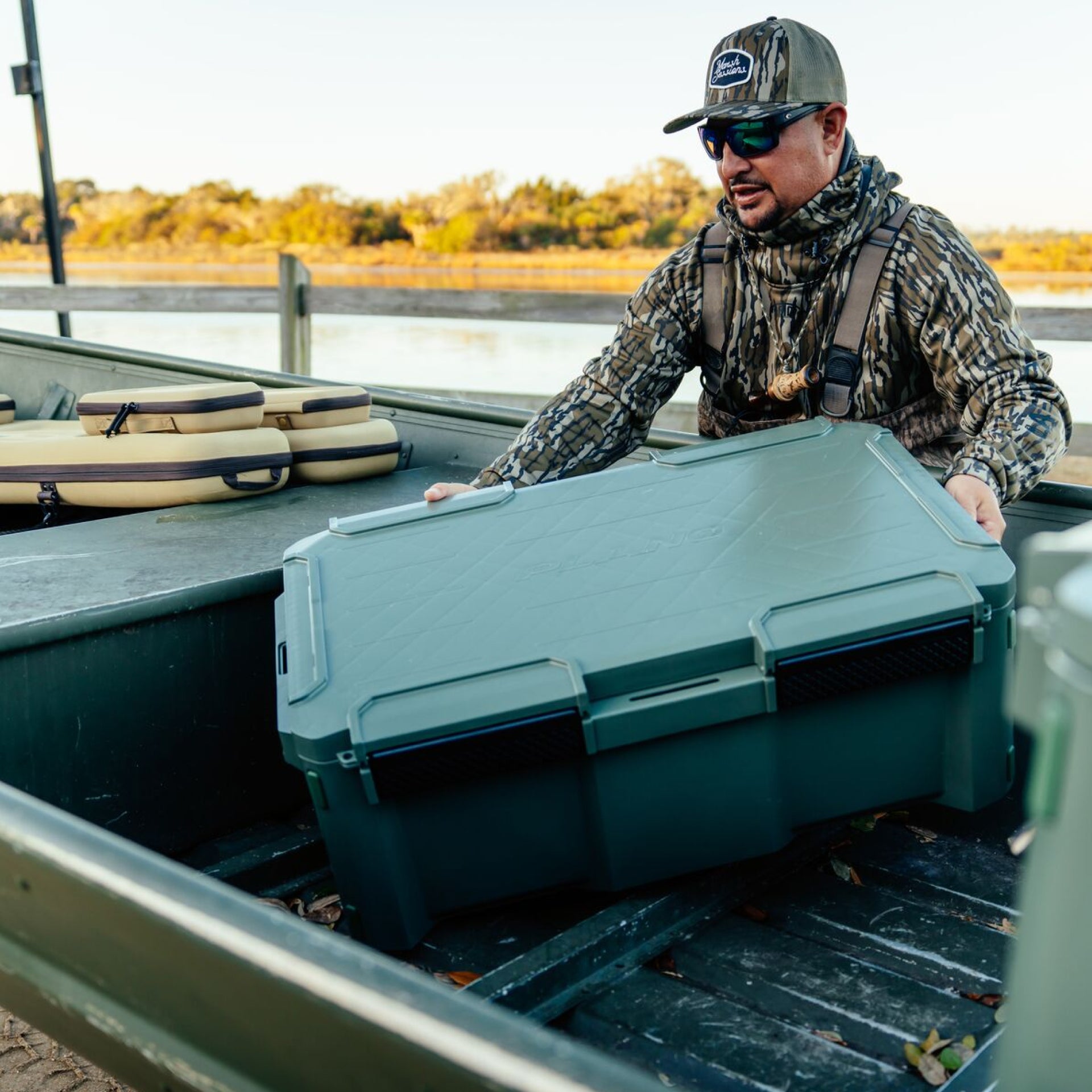 Man in camouflage gear opening a green cooler on a boat