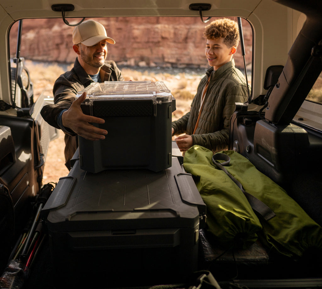 Two people loading camping gear into a vehicle with a scenic background