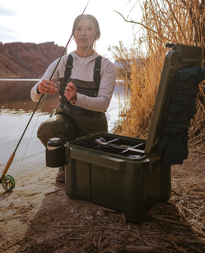 Person fishing by a lake with a green cooler box open