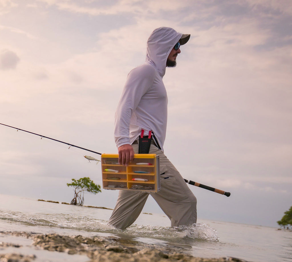 Man walking on a beach with a fishing rod and tackle box