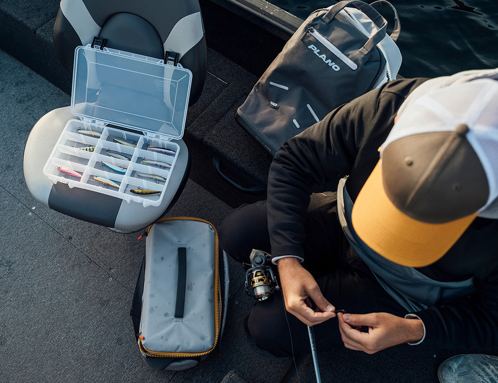 Person preparing fishing gear with a tackle box and bag in a vehicle.