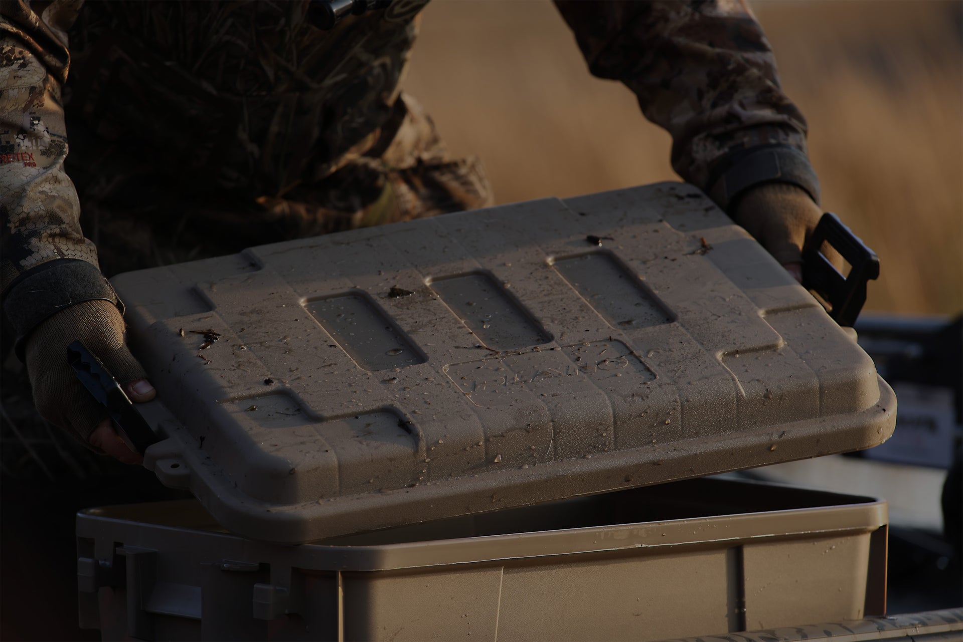 Person holding a tactical box with a camouflage pattern in a natural setting