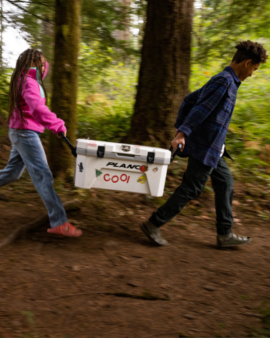 kids carrying white plano cooler in woods